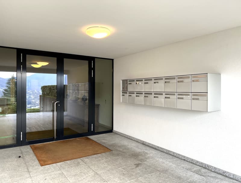 Entrance with glass doors, brown rug, white wall, mailboxes, ceiling light, tiled floor