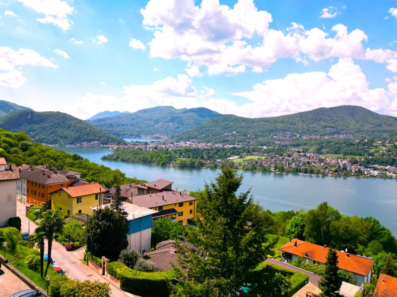 Aerial view of a hillside town with houses, mountains, and a lake in the background