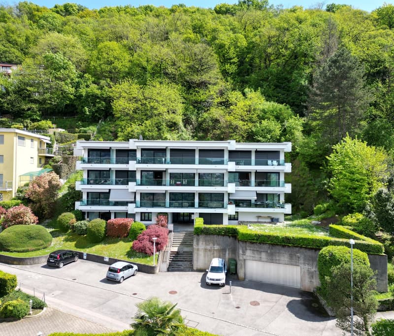 3 story apartment building, white exterior, large windows, balconies, parking area, green surroundings