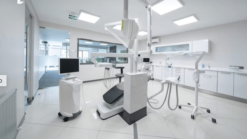 Modern and clean dental office with white walls, tiled floor, dental equipment such as chairs, monitors, and other medical devices.