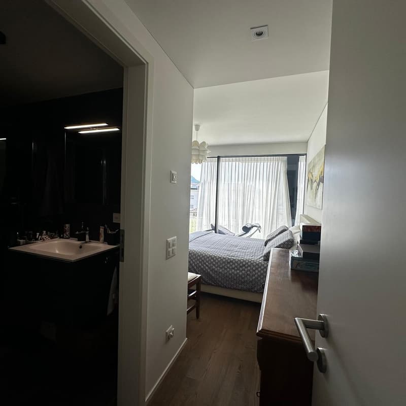 Bedroom with large windows, hardwood floors, and a bathroom visible through the doorway