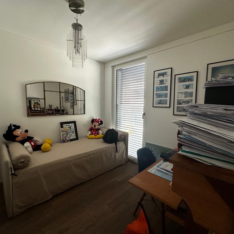 Bedroom with large window, couch, shelves with framed artwork, and stuffed animal toys