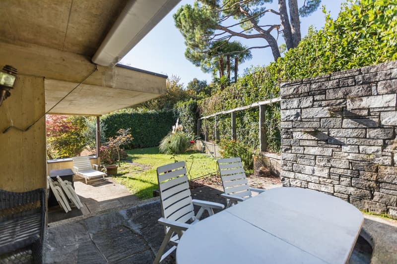 stone patio, outdoor dining table, chairs, stone wall, garden with greenery and flowers
