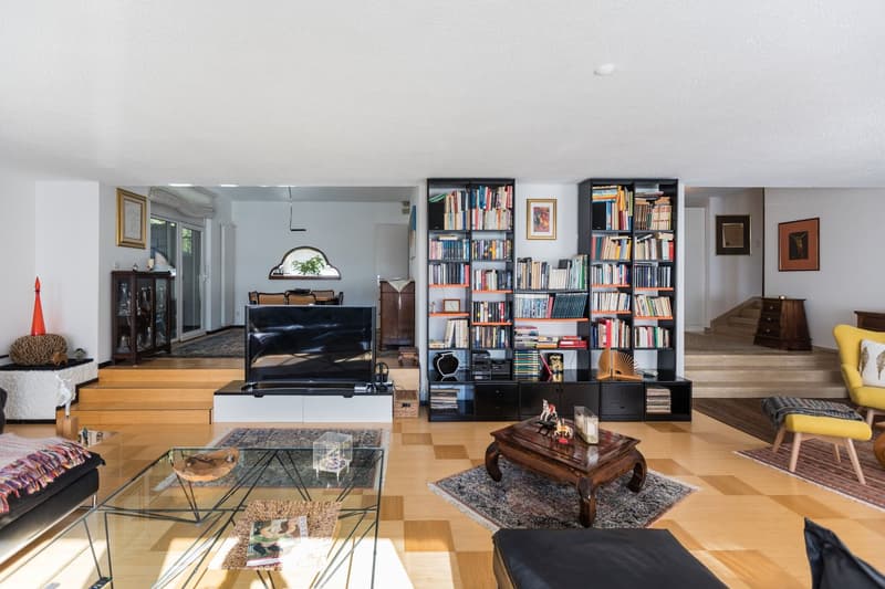 large room, hardwood floors, bookshelves, flat screen TV, coffee table, large rug, armchairs