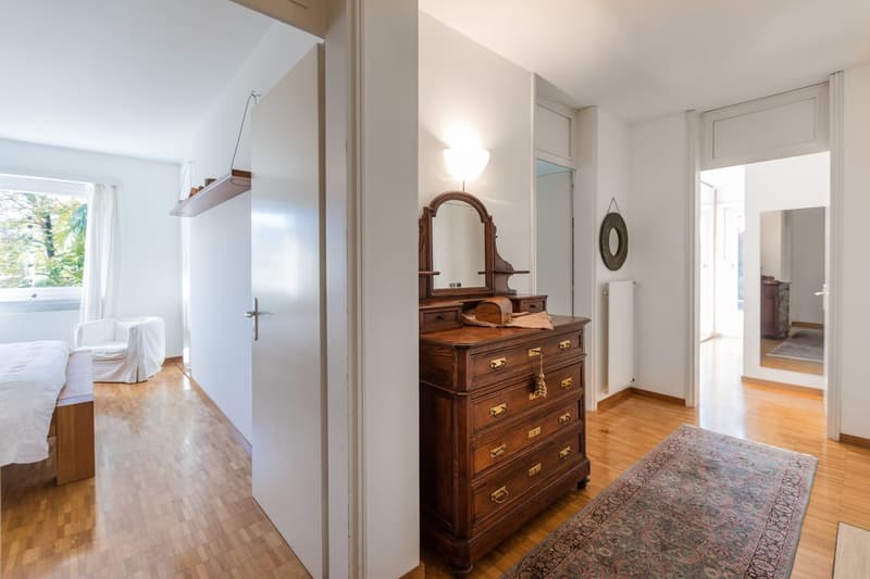 room with hardwood floor, large mirror, wooden dresser, rug, bedside chair