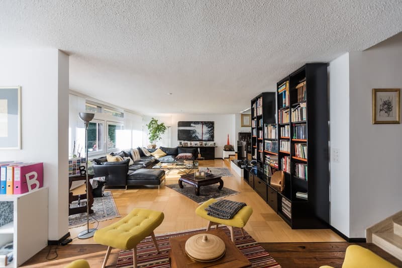 living room with black sofa, coffee table, shelves, lamp, two yellow chairs, wooden floor, white walls