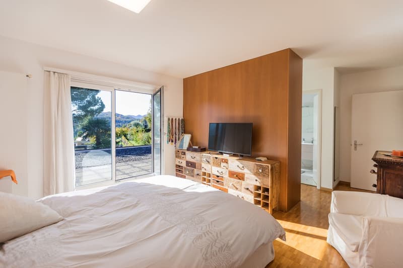 large bed, wooden chest of drawers, flat screen TV, sliding glass door, balcony, white walls, wooden floor