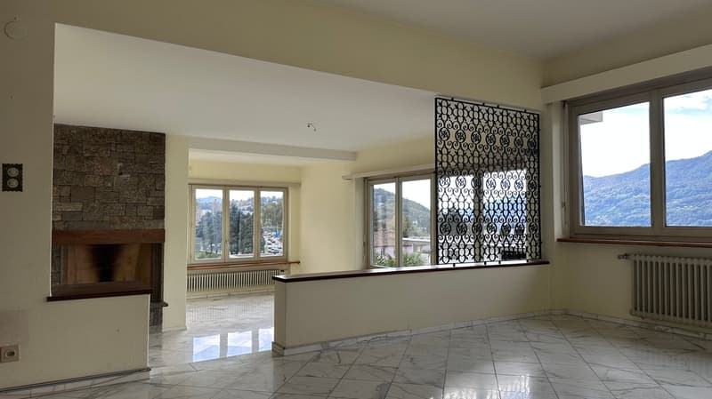 Spacious living room with large windows, stone fireplace, and decorative metal screen divider. The room has a tiled floor and neutral-colored walls.