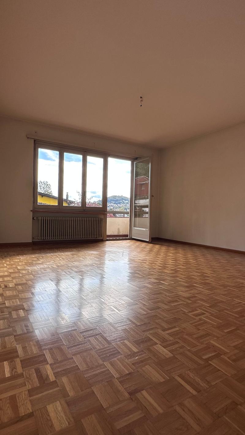 Spacious room with large windows, hardwood parquet flooring, and a balcony or terrace overlooking the surrounding area.