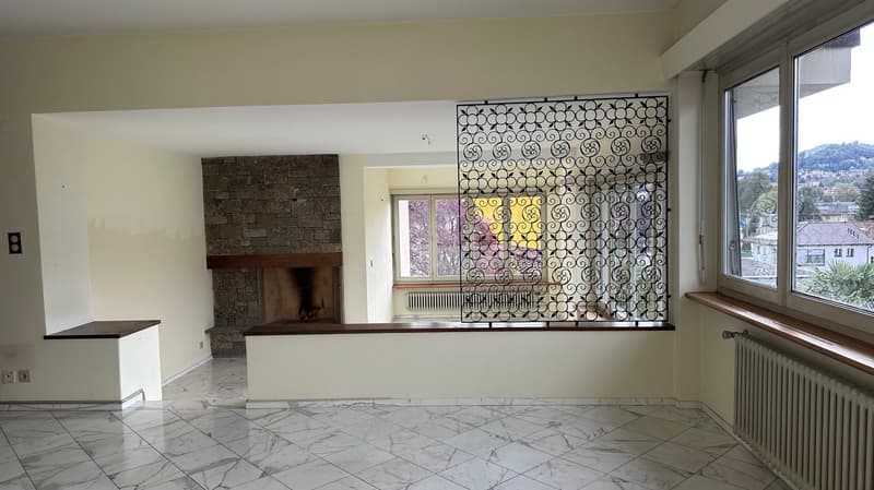 Spacious living room with a stone fireplace, large windows, and a decorative metal screen divider. The room has marble flooring and a minimalist design.