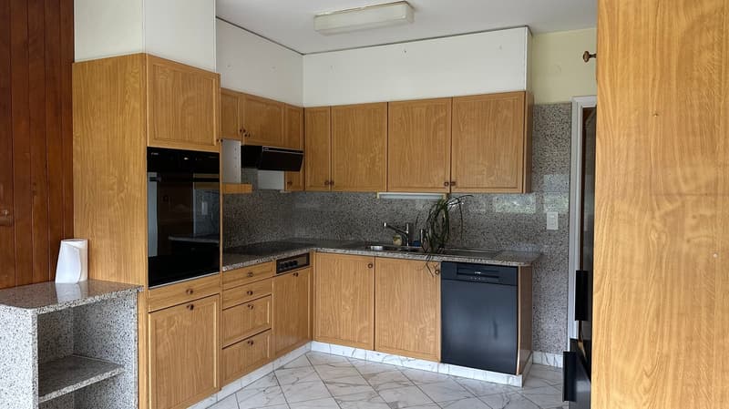 The image shows a kitchen with oak wood cabinets, granite countertops, a dishwasher, and tile flooring.