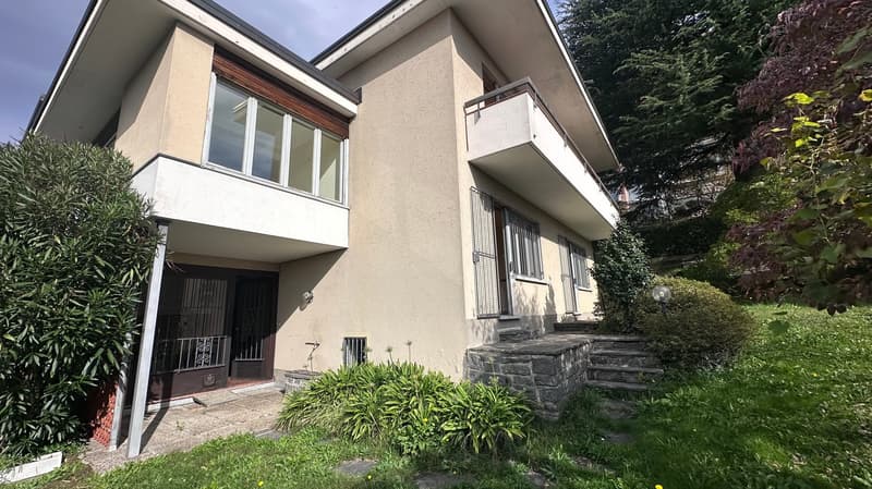 2-story house with stucco exterior, large windows, balcony, and landscaped garden with stone steps leading to the entrance.