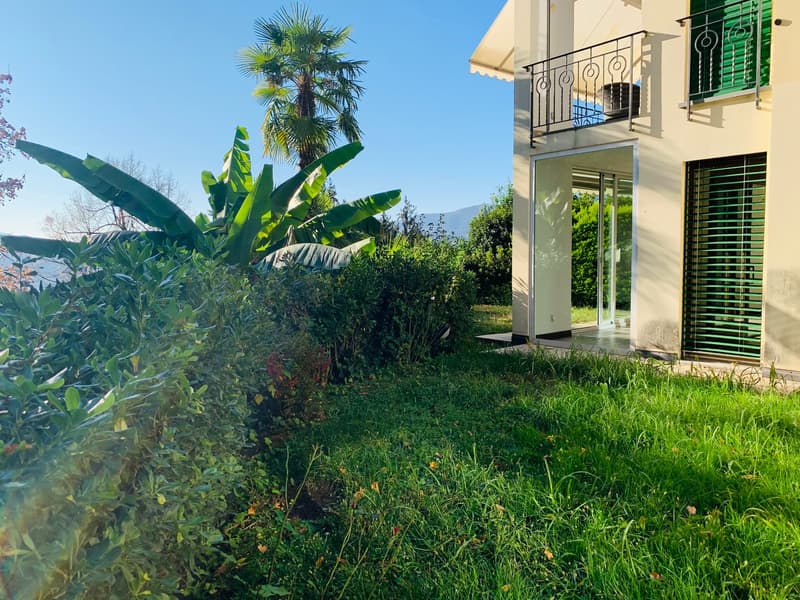 A house with a balcony, surrounded by greenery, glass doors, and plants
