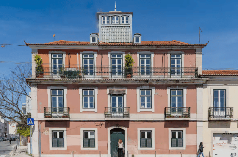 multi story building, red roof, pink walls, multiple balconies, large windows