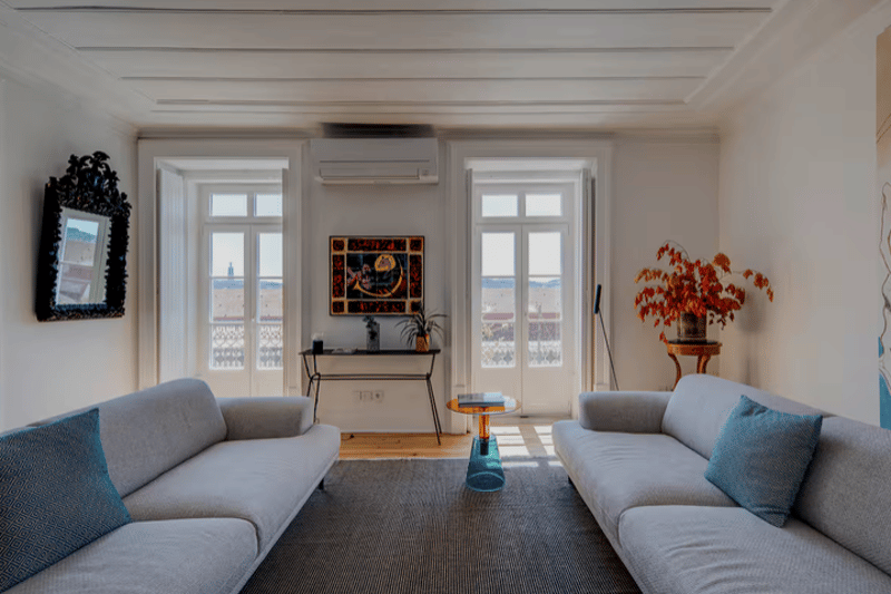 living room with two sofas, carpet, side table, mirror, painting, plant, window