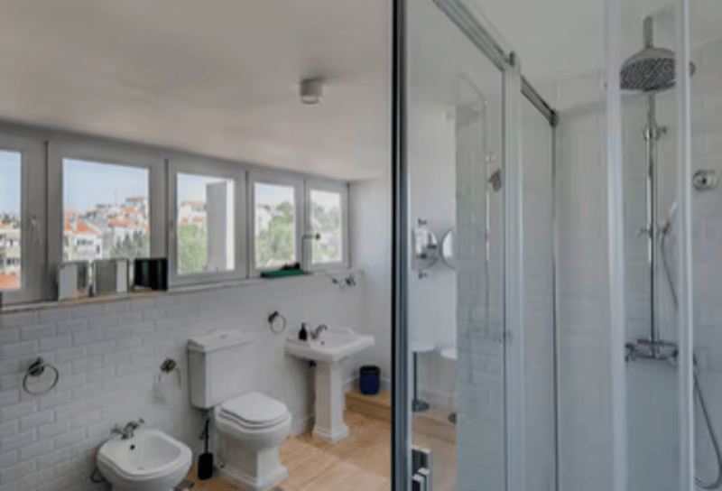 white tiles, white porcelain toilet, white bidet, pedestal sink, shower with glass door
