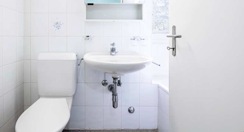 A white tiled bathroom with a toilet and a white sink
