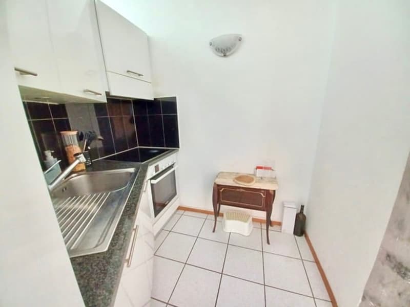 white cabinets, tile floor, stainless steel sink, black countertop, white oven, small wooden table