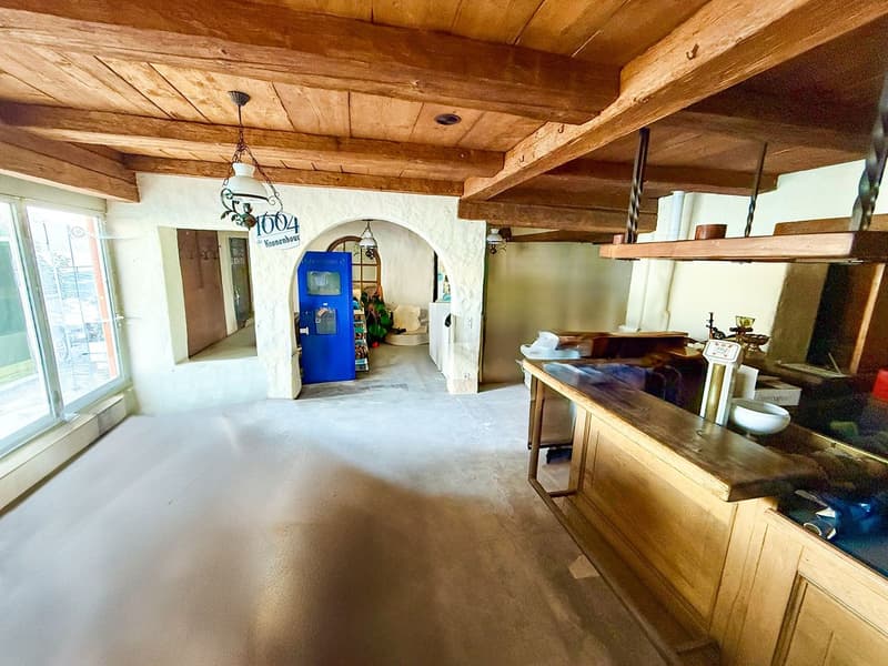 White walls, wooden beams, white floor, blue door, wooden counter, lamps, window with glass door