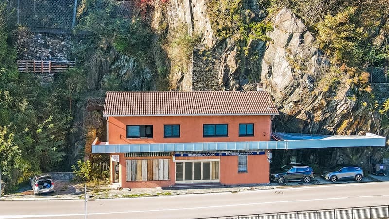 2 story building, terracotta roof, orange paint, 5 windows, cars parked, next to cliff