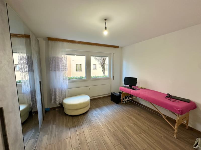 empty room, wooden flooring, white walls, full length mirror, white curtains, white ottoman, pink massage table, computer and keyboard, large window
