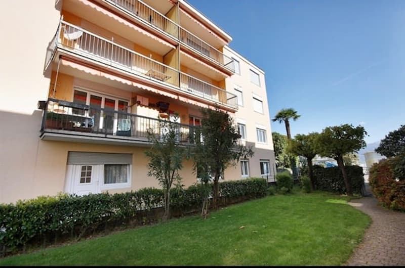Modern apartment building with yellow walls, large balconies, and lush green gardens