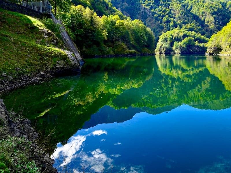 lake with reflections, trees around, hills, and a small fence along the slope