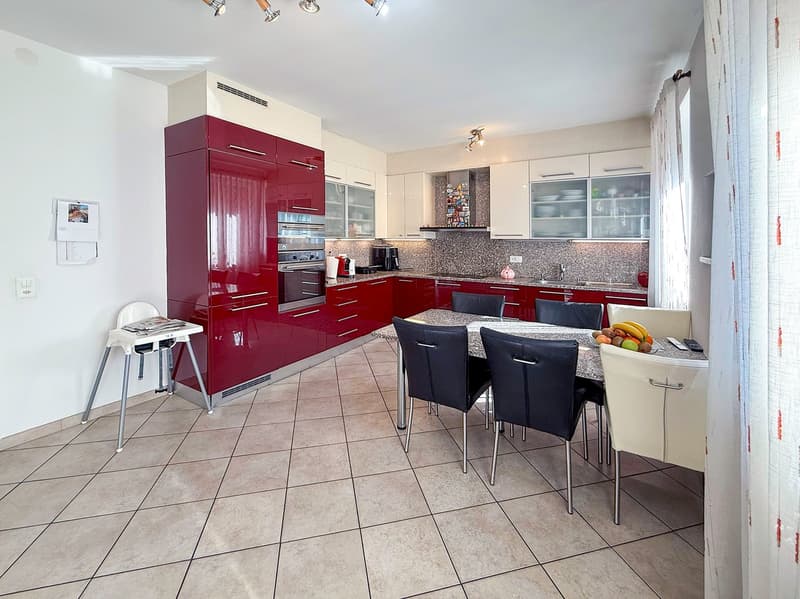 Spacious kitchen with red glossy cabinets, granite countertops, stainless steel appliances including a dishwasher, and a dining table with black chairs