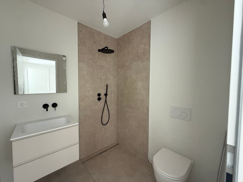 modern bathroom with white walls, white sink, white toilet, mirror, shower, power outlet, light bulb