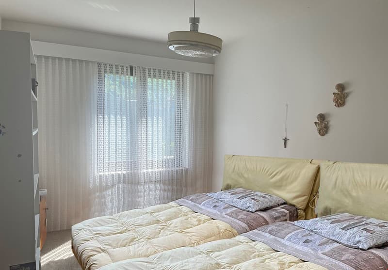 Spacious bedroom with large window, sheer curtains, pendant light fixture, bed with bedding, and wall decor