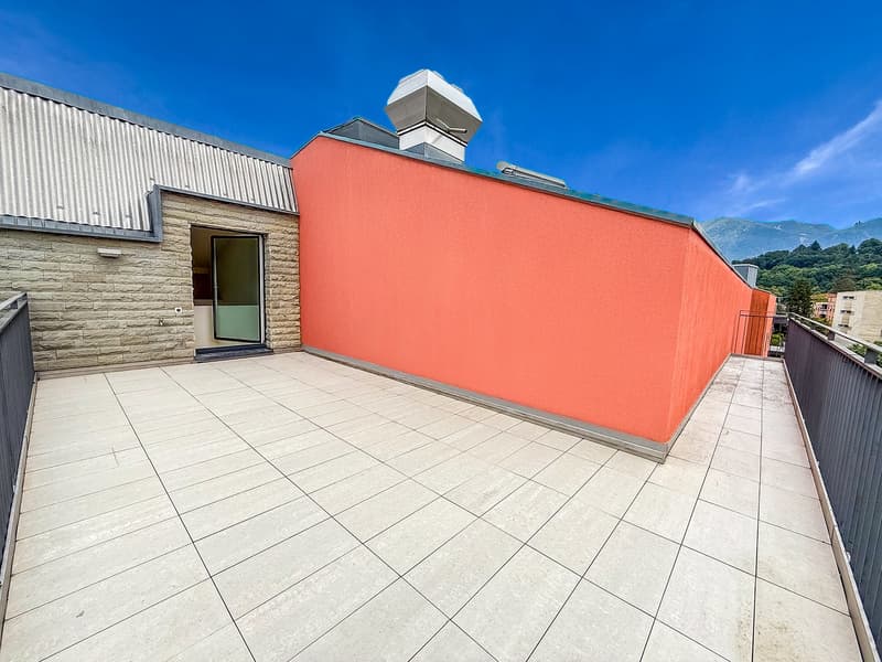 Spacious balcony with tiled flooring, orange exterior wall, and a ventilation system on the roof.