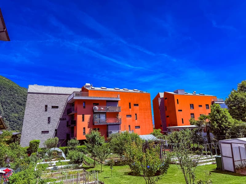 Multi-story apartment building with vibrant orange and purple facades, surrounded by lush greenery and landscaping, with visible balconies on the upper floors.