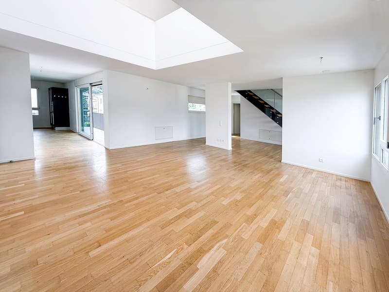 Spacious open-concept living area with hardwood flooring, white walls, and a large skylight providing natural light. The room has a clean, minimalist design with no visible furniture or decor.