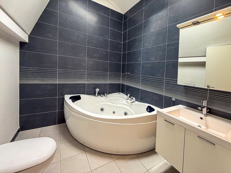 Large corner bathtub with jets, black and white tiled walls, vanity with sink, and toilet