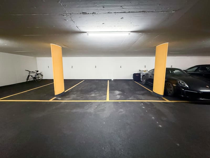 Underground parking garage with numbered parking spots, concrete floor, yellow support columns, and a bicycle parked in one of the spots.
