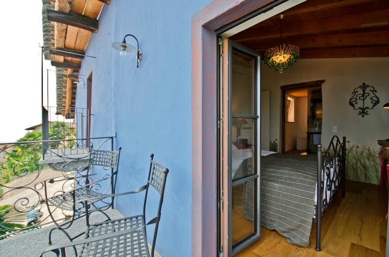 Outdoor patio area with wrought iron furniture, blue exterior wall, wooden beams on the ceiling, ornate light fixture, and a doorway leading into the interior of the home.