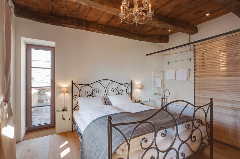 Rustic bedroom with wooden beamed ceiling, iron bed frame, chandelier, and access to a balcony or terrace