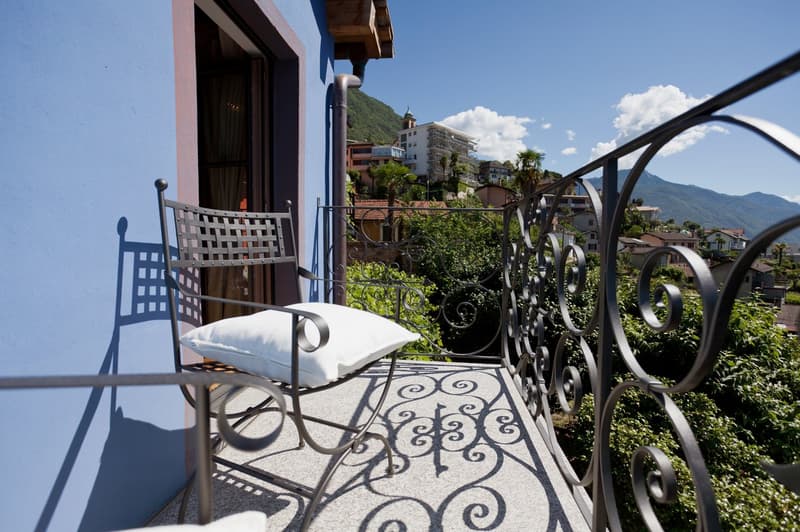 Balcony with wrought iron railing, wicker chair, and view of surrounding buildings and mountains