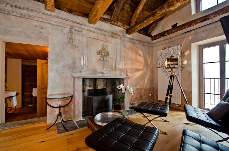 Rustic living room with exposed wooden beams, stone fireplace, leather furniture, and decorative lighting fixtures
