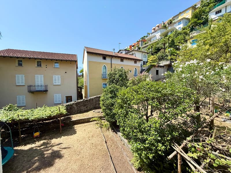 Yellow house, red roof, large windows, balcony, outdoor swing, surrounded by greenery and hillside homes