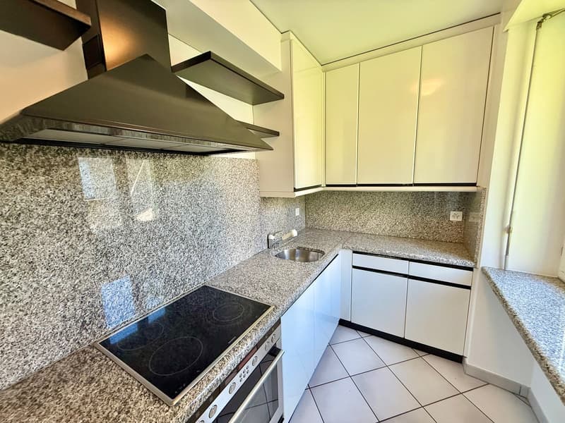 White tile flooring, white cabinets, granite countertops, black stove, black range hood, silver sink, under-counter power outlet