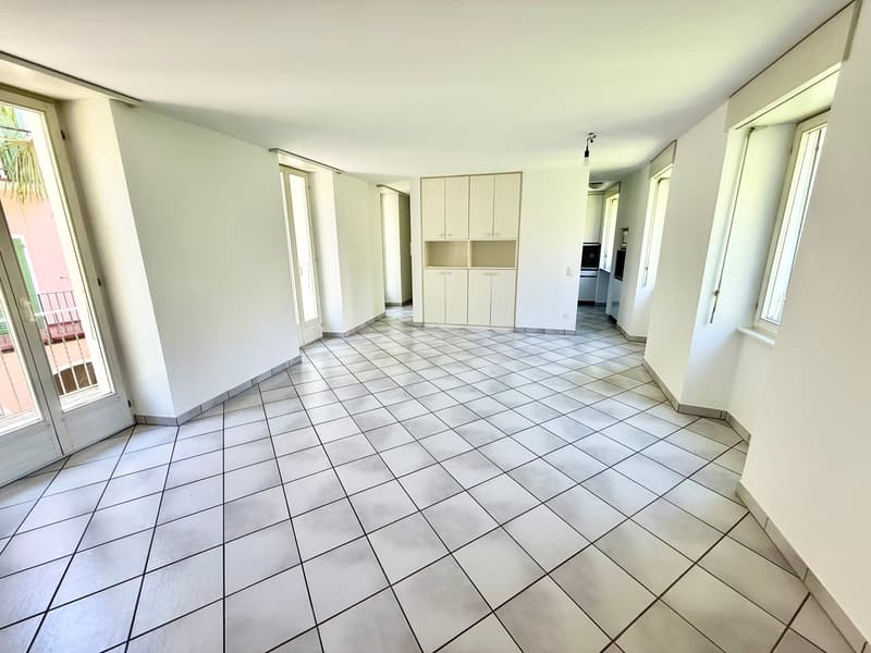 Empty room with white tile flooring, white walls, sliding glass doors, windows, built-in white cabinets, ceiling lamp
