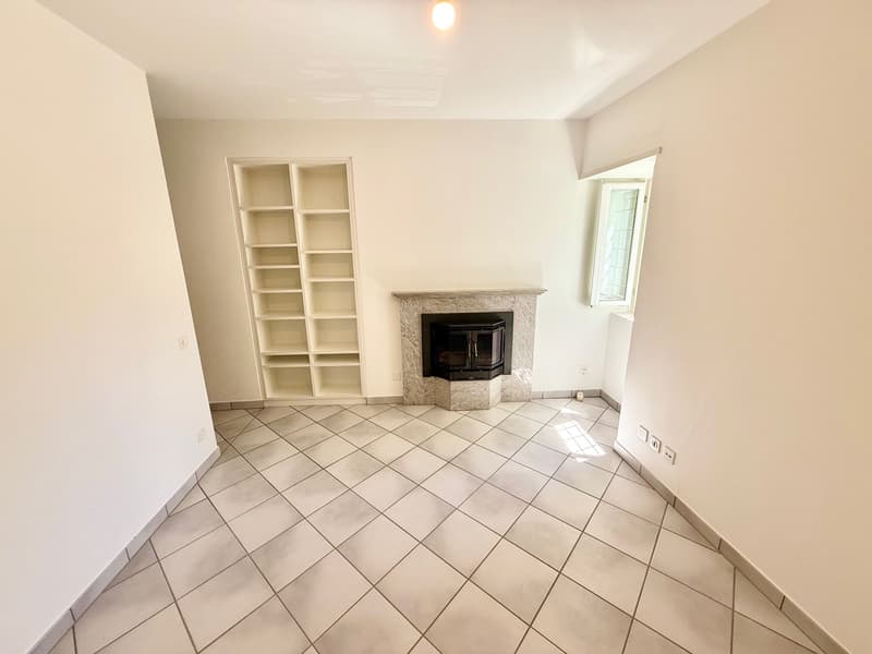 Empty room with white tiled floor, white walls, fireplace, built-in shelves, and a small window.