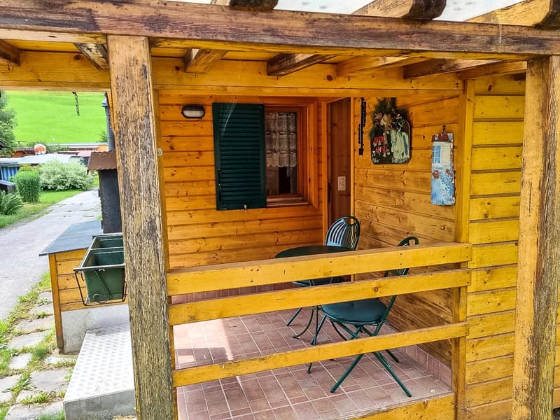 Yellow wooden walls, table and chairs on the porch, green plant hanging from wall