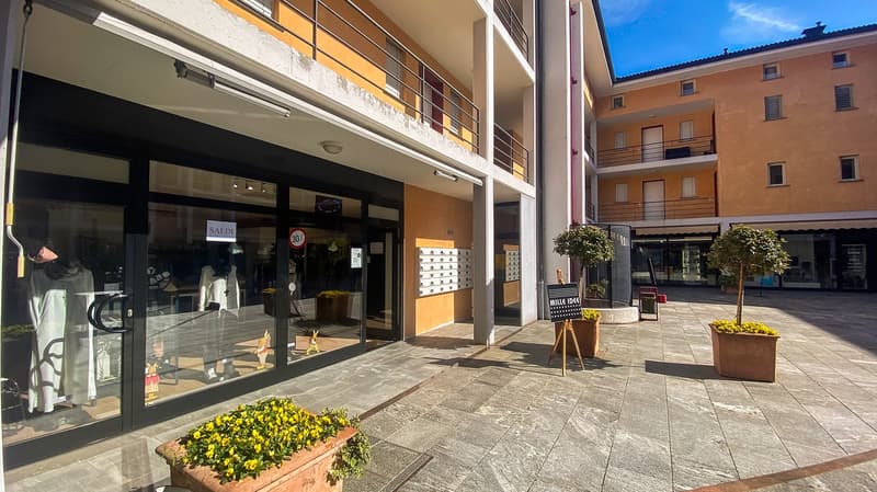 Facade of a multistory building with balcony, shops, and outdoor area with trees and plants