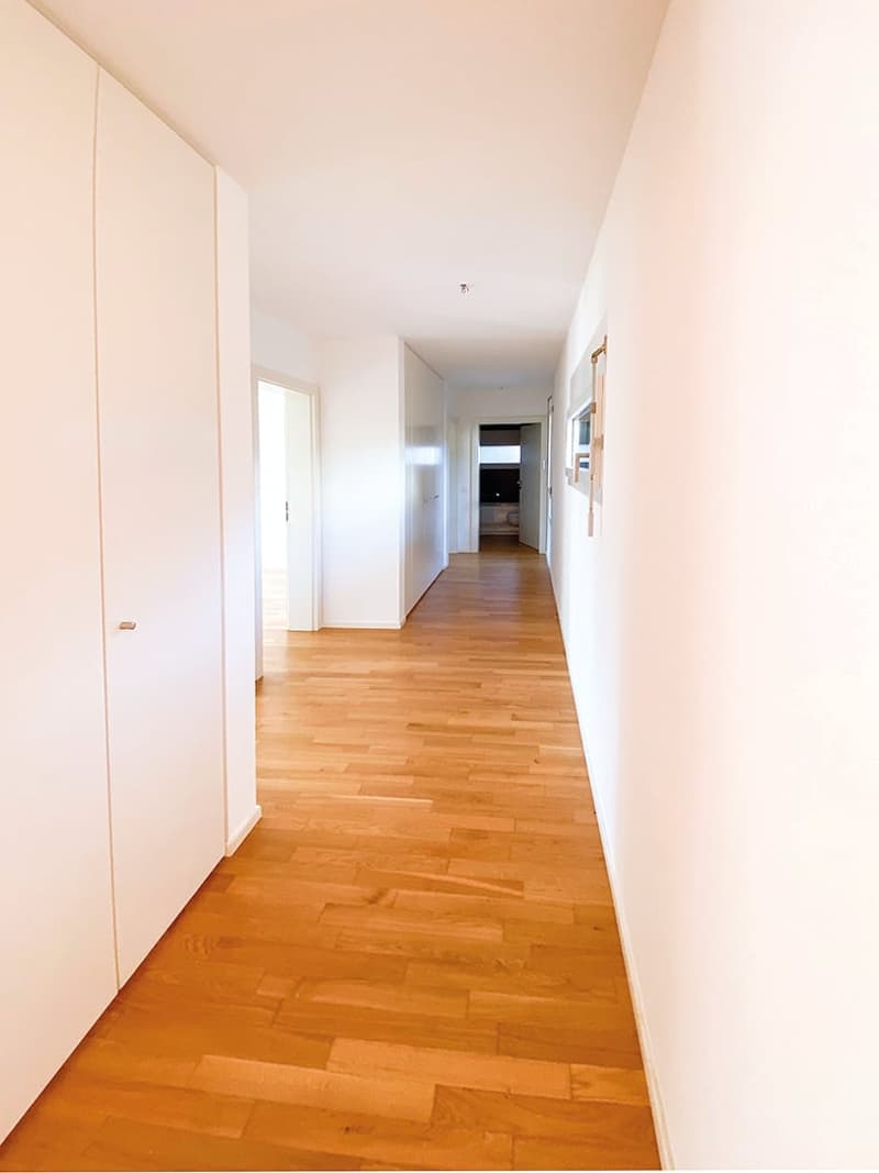 Empty hallway with wooden floor, white walls, and doors on both sides