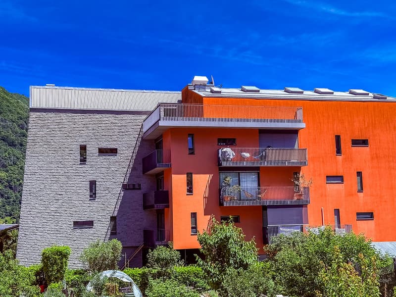 4-storey building, modern design, red and gray exterior, multiple balconies with plants, solar panels on roof