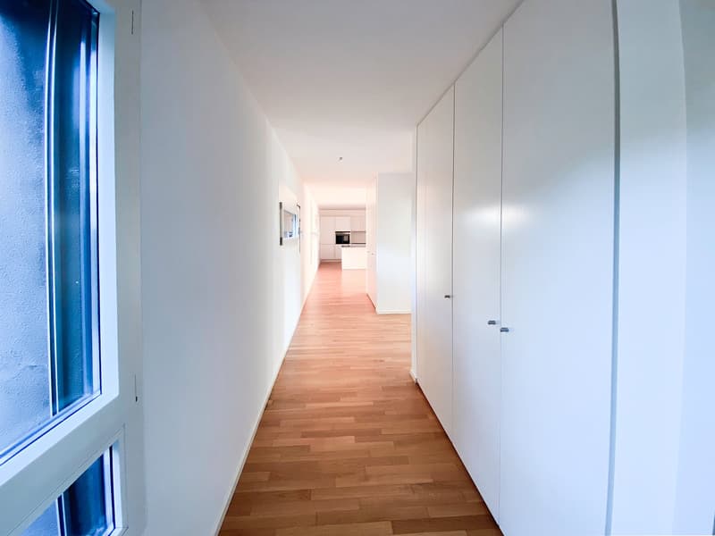 Empty hallway with wooden floor, white walls, and white cabinets