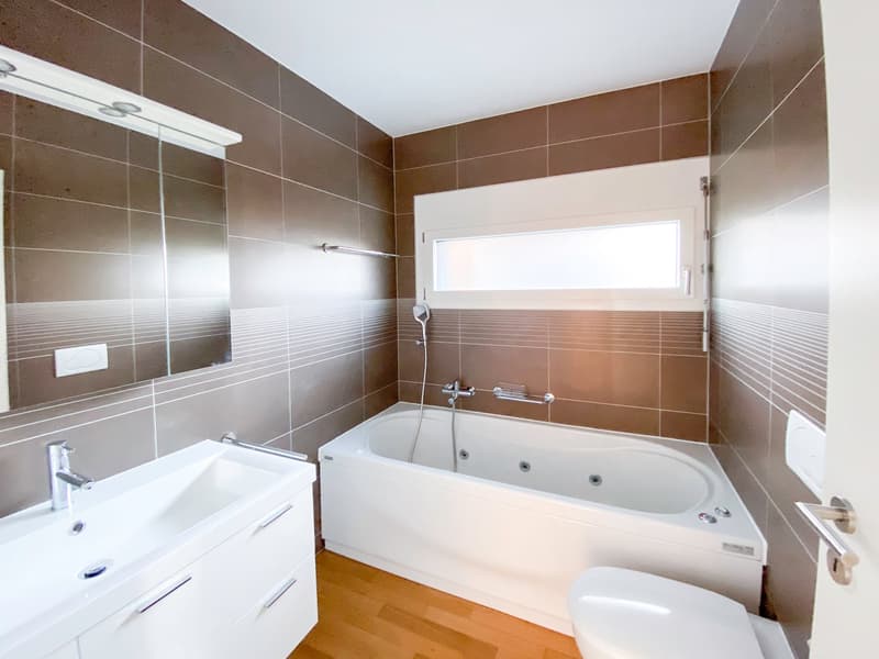 modern bathroom with brown tiles, white bathtub, white sink, white toilet, mirror, wooden floor