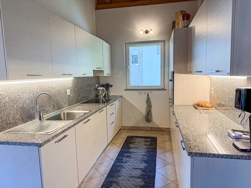 modern kitchen, granite countertops, stainless steel sink, built-in oven, white cabinets, microwave, sink with faucet, towel hanging on the wall, bread on a tray, and electrical outlets